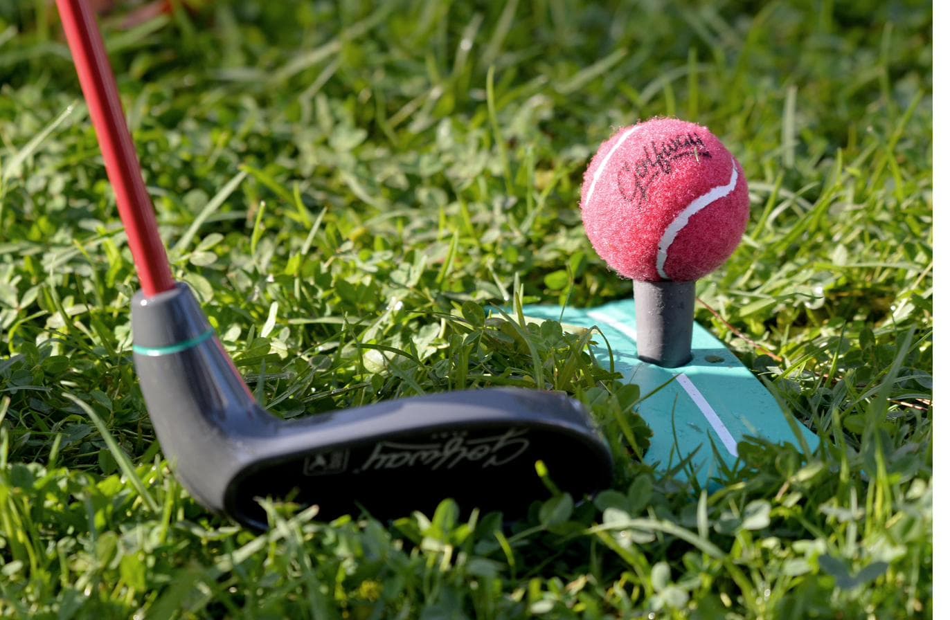 A soft pink Golfway felt ball on a rubber tee beside a junior golf club.